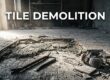 Lifted tile reveals mortar, wire reinforcement, and concrete beside demolition tools.